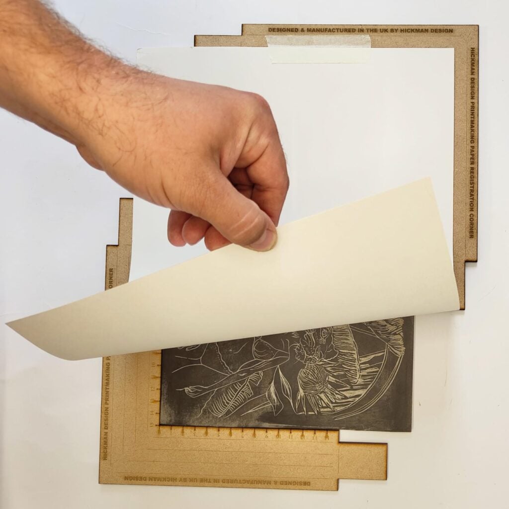 Lifting a print from a lino block positioned between registration corners
