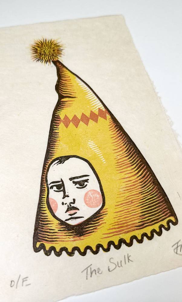 Close-up of The Sulk linocut by Gemma Trickey: a sulky face inside a tall yellow pointed hat, printed on textured handmade paper.